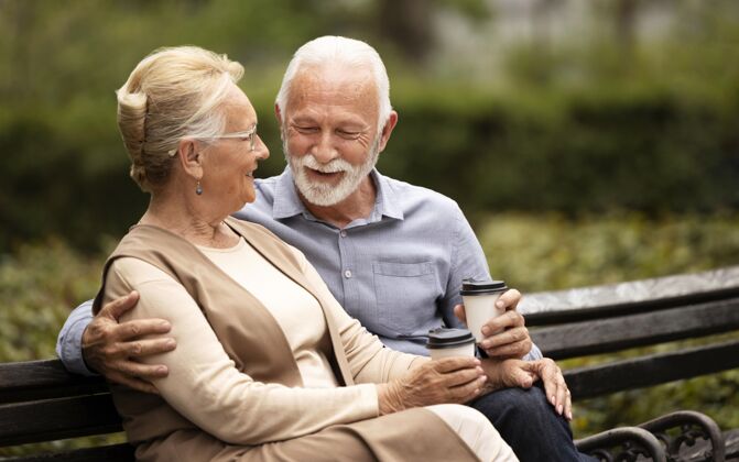 退休拿着杯子坐在长凳上的中枪老夫妇浪漫关系在一起