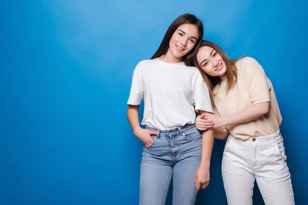 友谊两个快乐的女朋友被隔离在蓝色的墙上夏天耳语模特