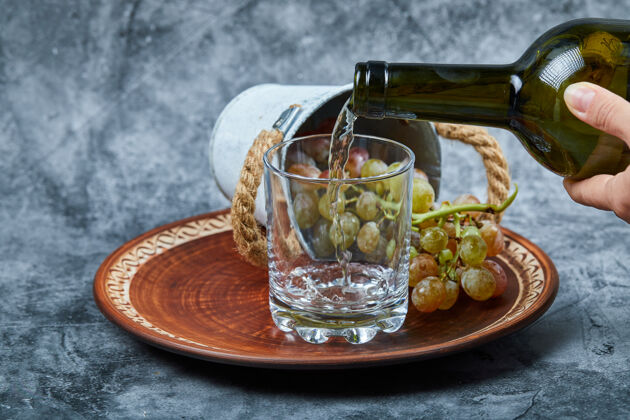 食物小桶的葡萄放在陶瓷盘上 用手把碗倒在玻璃上的大理石上收获瓶子盘子