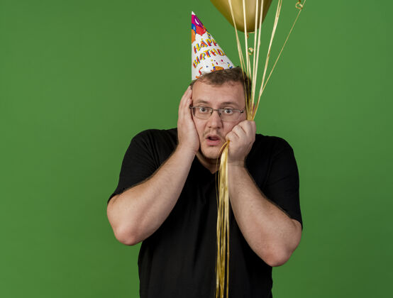 生日焦急的成年斯拉夫人戴着眼镜 戴着生日帽 手放在脸上 手里拿着氦气球帽子男人气球