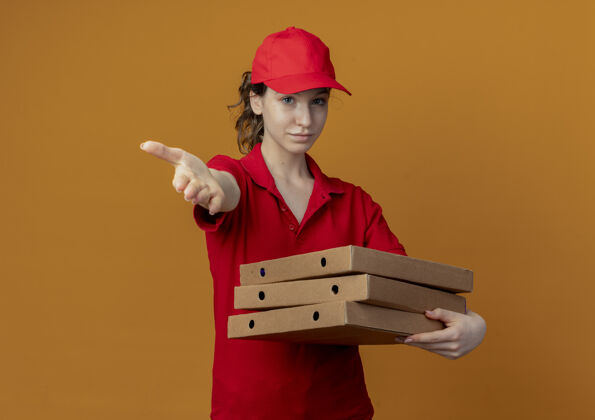 橙色自信的年轻漂亮的送货女孩 身穿红色制服 头戴鸭舌帽 手里拿着披萨包 向镜头伸出手走向红色女孩
