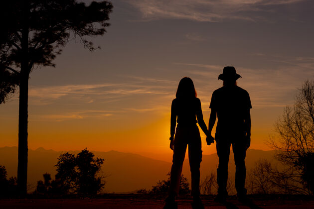 日落在山上欣赏日落的年轻夫妇剪影男性相聚