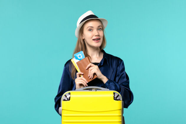 微笑正面图年轻女子拿着机票 准备在蓝色背景的飞机上度假海上度假旅行秘书抱准备