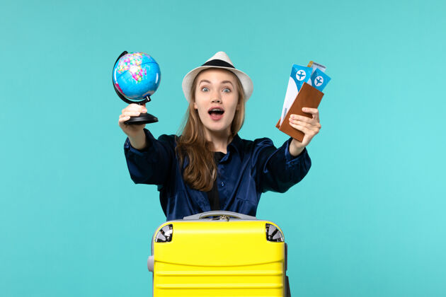 成人正面图年轻女子拿着机票和小地球仪在蓝色办公桌上乘机度假远航举行玩地球