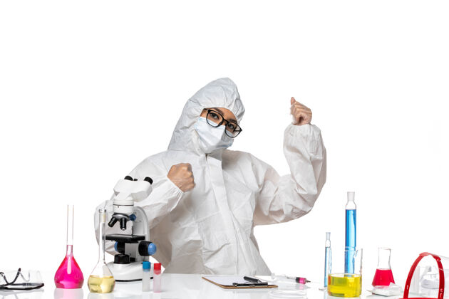 医生正面图年轻的女化学家穿着特殊的防护服 坐在桌子前 用浅白背景病毒的解决方案实验室的covid健康化学病毒实验室西装