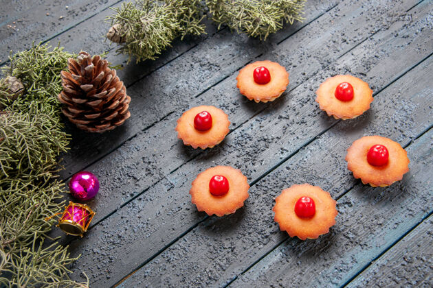 圆锥体底部视图圆形樱桃纸杯蛋糕冷杉树枝圣诞玩具和一个圆锥在黑暗的木制地面水果地圣诞节