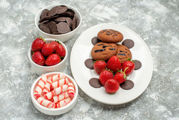 中间底视图巧克力饼干草莓和圆形巧克力放在白色椭圆形盘子上 碗里放着糖果草莓巧克力放在灰白色的桌子中央草莓巧克力浆果