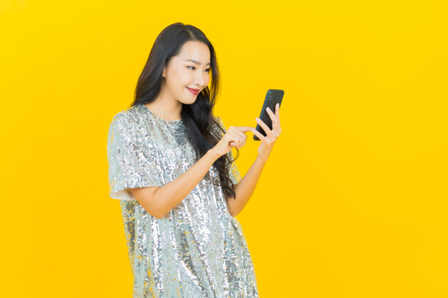 休闲肖像美丽的亚洲年轻女子微笑着智能手机上的黄色电话信息电话