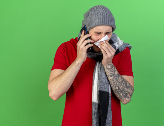疾病一个戴着冬帽 戴着围巾 用纸巾擦鼻子的年轻白种人在格林街打电话穿绿色男人