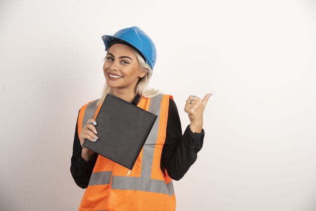 成人面带微笑的工人拿着笔记本在白色背景上竖起大拇指高质量的照片女孩安全帽女性
