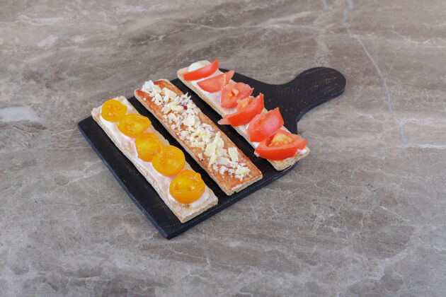Puf把熟的和未熟的西红柿切成薄片 放在切菜板上的酥皮面包上 放在大理石表面大米健康胡萝卜