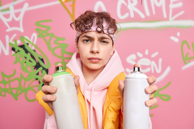 气溶胶横拍不开心的小伙子穿着运动衫拿着两个喷雾瓶在街上创造性地涂鸦有不满的表情青年成人消极