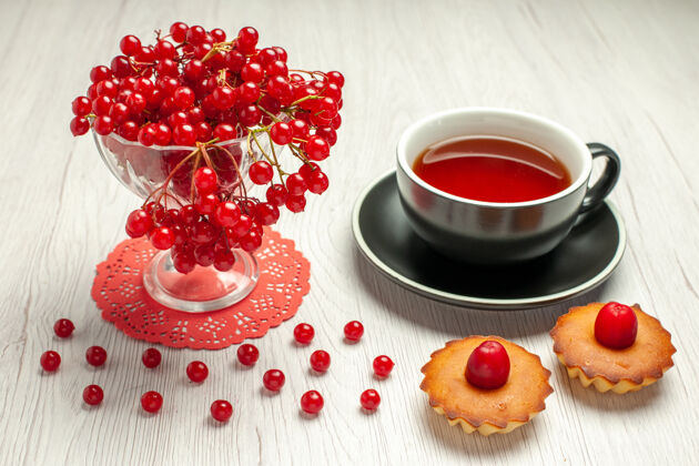 红醋栗正面图红色椭圆形蕾丝桌布上的水晶杯里的红醋栗 白色木桌上的一杯茶和馅饼水晶餐浆果