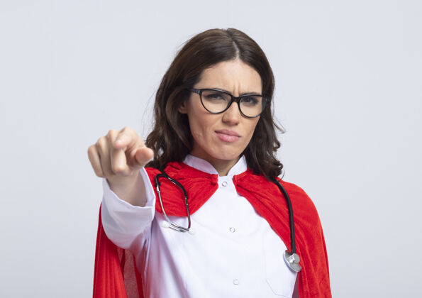 医生严肃的女超人穿着医生制服 戴着红色斗篷 听诊器戴着光学眼镜 前面的白色墙壁上孤立着几点光学斗篷脸