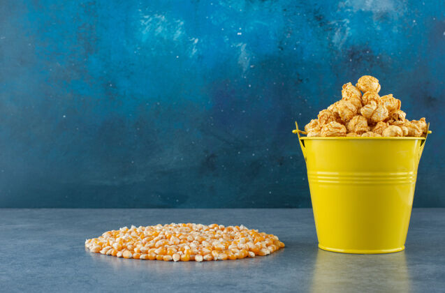 小吃黄色的爆米花糖桶旁边是一堆整齐的玉米粒 蓝色的好吃桶装好吃
