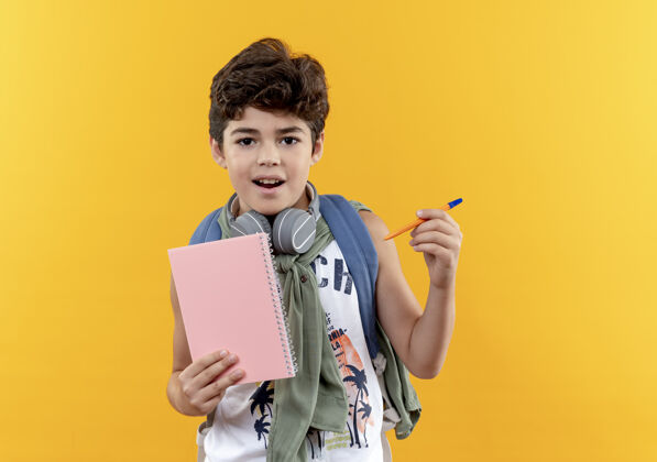 小男孩高兴的小男生背着书包戴着耳机拿着笔记本拿着笔黄色笔请