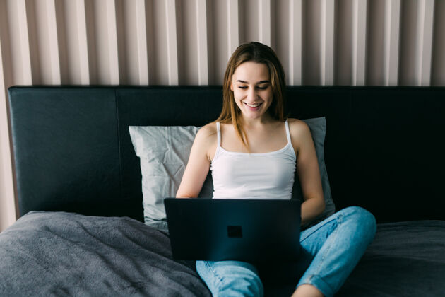 穿着懒洋洋地躺在床上用笔记本电脑休息时 一个微笑着的女人在社交媒体上忙得不可开交床笔记本电脑腿