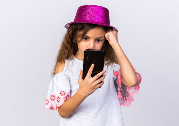 电话焦急的小白种女孩 戴着紫色派对帽 手放在额头上 手拿着手机 看着隔离在白色墙壁上的手机 还有复印空间生日抱小