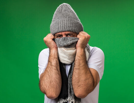 疾病疼痛的成年白种人 戴着冬天的帽子 用围巾遮住脸 隔离在绿色的墙上 留着复印空间盖白种人成人