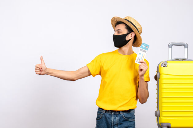 稻草正面图：戴草帽的年轻人站在黄色手提箱旁 手里拿着旅行票 指着拇指朝上的牌子男人指向拇指