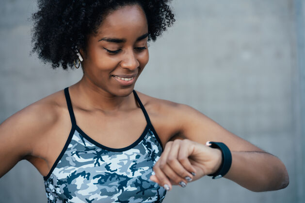运动一个黑人运动妇女在户外锻炼时用智能手表查看时间耳塞设备检查