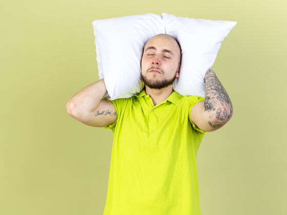 姿势昏昏欲睡的年轻病人把枕头放在脖子后面 隔离在橄榄绿的墙上人人脸