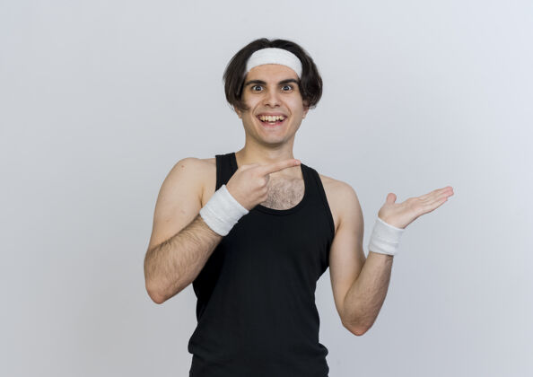 运动装身穿运动服 头戴头巾的年轻人站在白色的墙壁上 用食指指着侧面 愉快地微笑着人头带感觉