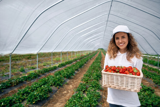 水果卷曲的黑发女人手里拿着一个装草莓的大篮子栽培农业帽子