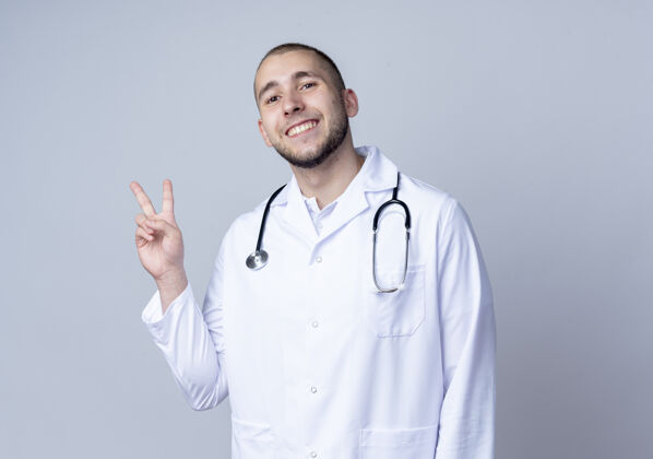 男性面带微笑的年轻男医生穿着医用长袍 戴着听诊器 脖子上挂着和平的牌子 隔离在白墙上长袍年轻人