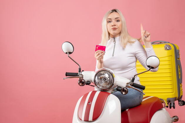坐着正面图：骑着轻便摩托车的年轻女士拿着卡片指着天花板优雅的粉色墙壁成人天花板轻便摩托车