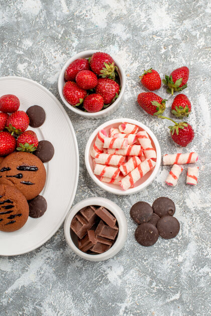碗白色椭圆形盘子上的饼干草莓和圆形巧克力灰白色桌子上的糖果草莓巧克力碗可食用的水果水果食物