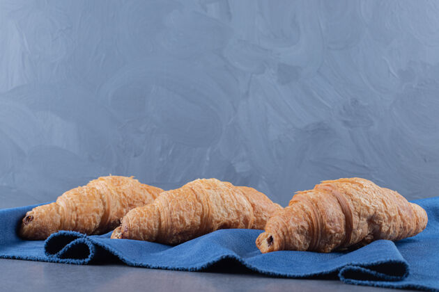 面包卷三个新鲜的法式羊角面包放在蓝色餐巾上餐有机羊角面包