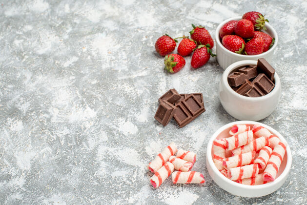 新鲜顶视图碗草莓巧克力糖果和一些草莓巧克力糖果在右边的灰白色马赛克表水果食品餐桌