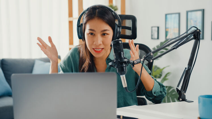 创作者快乐的亚洲女孩用耳机和麦克风在笔记本电脑上录制播客录音广播名人