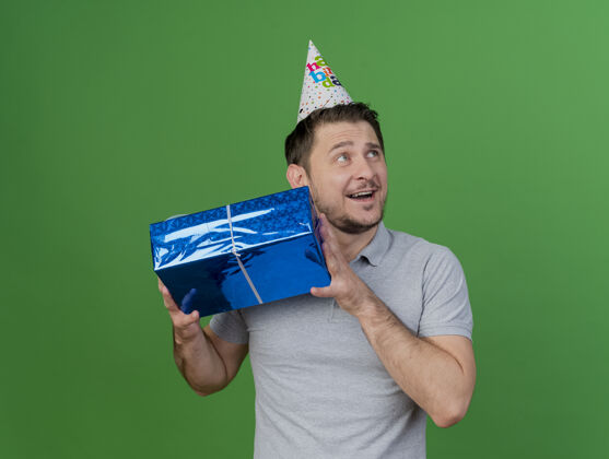 生日微笑的年轻人戴着生日帽拿着礼品盒孤立在绿色壁板绿色聚会