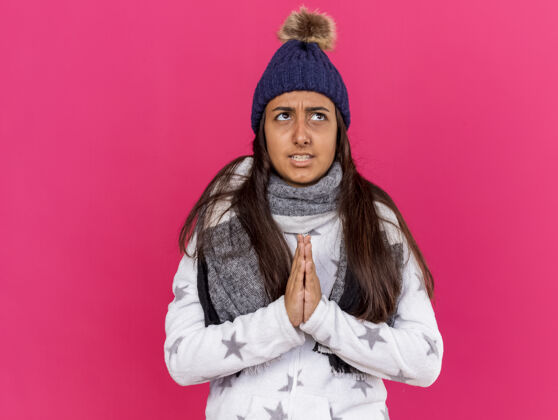 围巾关心生病的年轻女孩 戴着冬天的帽子 戴着粉色的围巾祈祷显示手势