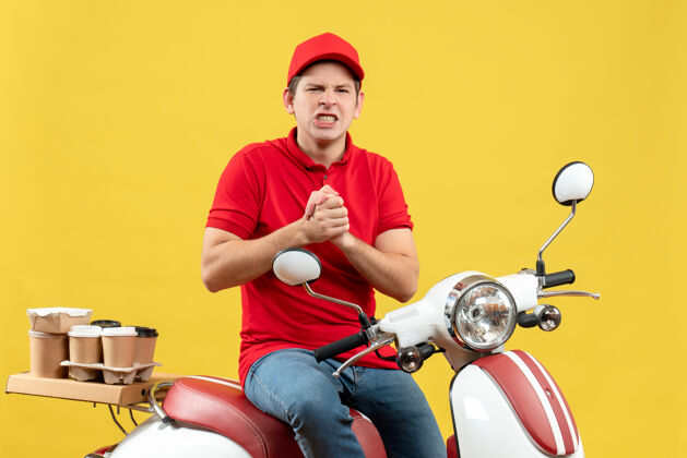 送货顶视图紧张的年轻人穿着红色上衣 戴着帽子 在黄色背景下传递命令男人年轻人摩托车