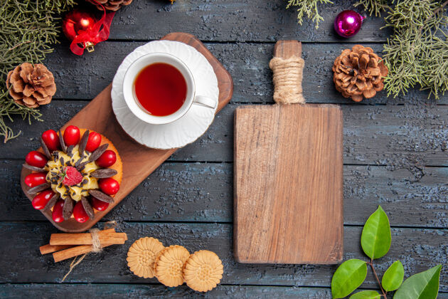 树叶顶视图一杯茶和浆果蛋糕放在木制盘子上松果圣诞玩具叶子和一个砧板放在深色的木制桌子上杯子盘子木板