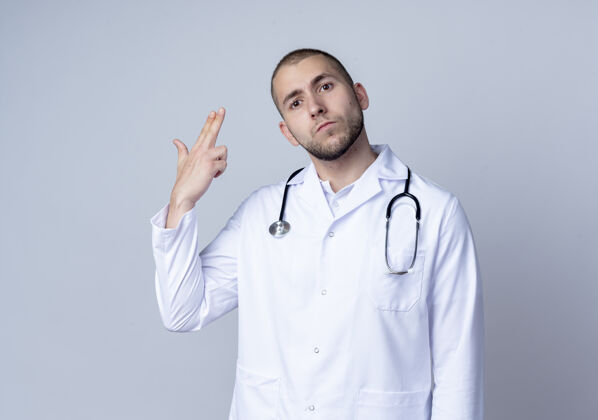 年轻面容严肃的年轻男医生 身穿医用长袍 脖子上戴着听诊器 手孤立在白墙上做着手势穿着脖子人