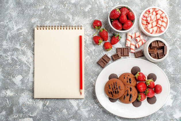 巧克力白色盘子上的曲奇草莓和圆形巧克力 灰白色地面上的糖果草莓巧克力和笔记本新鲜盘子研磨