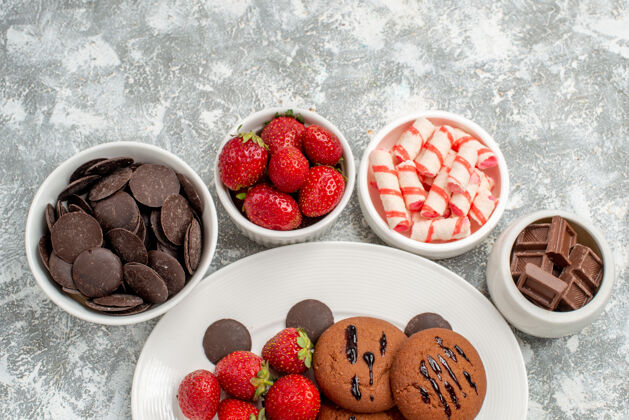 糖果上半部分是白色椭圆形盘子上的饼干 草莓和圆形巧克力 碗周围放着糖果 草莓和巧克力盘子椭圆形可食用水果