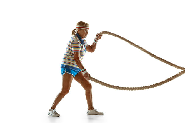 运动装穿运动服在白墙上用绳子训练的高级女子举行休闲动作