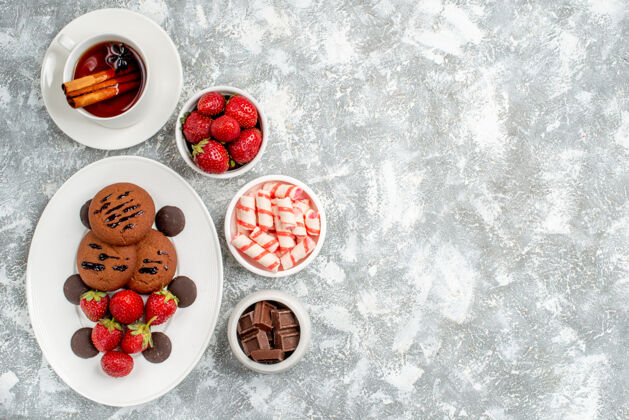 葡萄干顶视饼干草莓和圆形巧克力在椭圆形的盘子周围的糖果草莓巧克力肉桂茶碗在灰白色的桌子左侧桌子左边肉桂