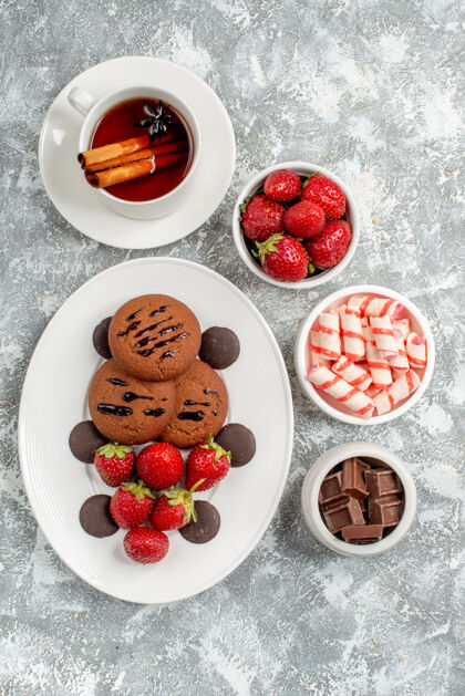 巧克力俯瞰饼干草莓和圆形巧克力放在椭圆形的盘子里 圆形的碗里放着糖果草莓巧克力肉桂茶放在灰白色的桌子上椭圆形碗草莓