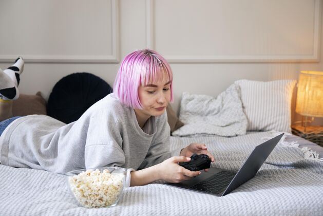 游戏粉红色头发的年轻女子在玩笔记本电脑上的操纵杆数字乐趣女人