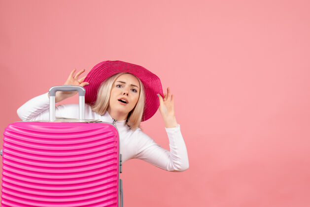 人正面图：站在手提箱后面戴着粉色巴拿马帽的金发女人快乐欢呼可爱