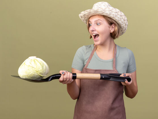 卷心菜兴奋的年轻的斯拉夫女园丁戴着园艺帽拿着铲在橄榄绿上的卷心菜斯拉夫兴奋橄榄
