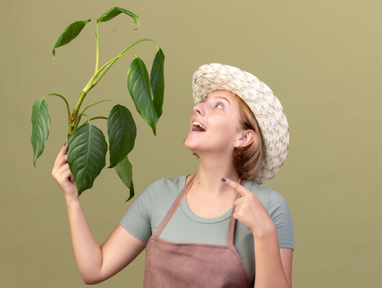 园艺快乐的年轻的斯拉夫女园丁戴着园艺帽 拿着橄榄绿看着植物花园橄榄欢乐
