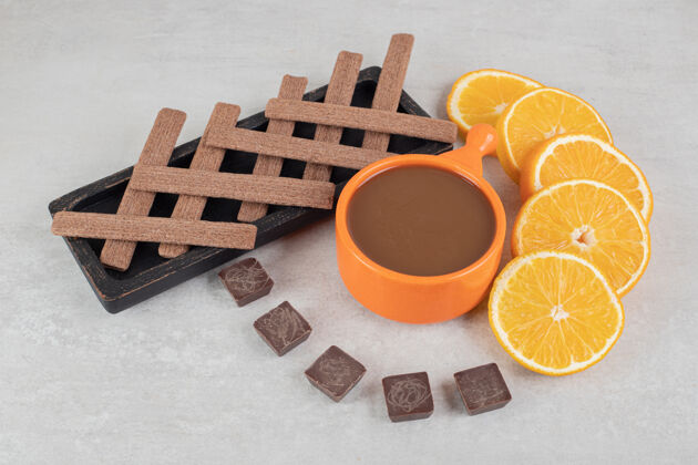 咖啡咖啡 橘子片 巧克力和饼干放在大理石表面杯子配料一餐