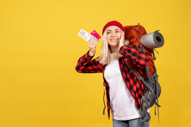 成人美丽的金发女孩背着背包 手里拿着卡片和旅行票背包肖像前面